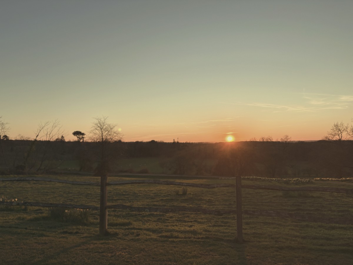Sunset over open fields with a wooden fence in the foreground